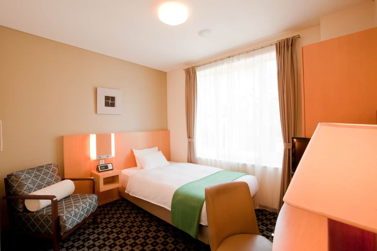 A hotel room with a bed, a chair, a desk, and a window with curtains.
