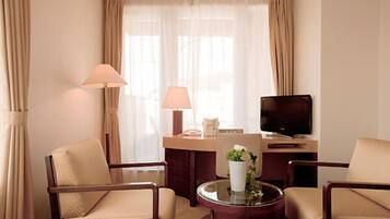 Habitación de hotel con dos sillones, un escritorio con televisor, una lámpara y un florero con flores.