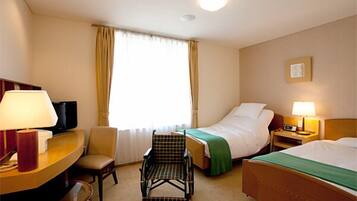 Quarto de hotel com cama, cadeira, escrivaninha com abajur, televisão e janela com cortinas.