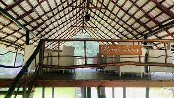 An open-air pavilion with a wooden roof structure and a sign reading "Peacock Lounge".