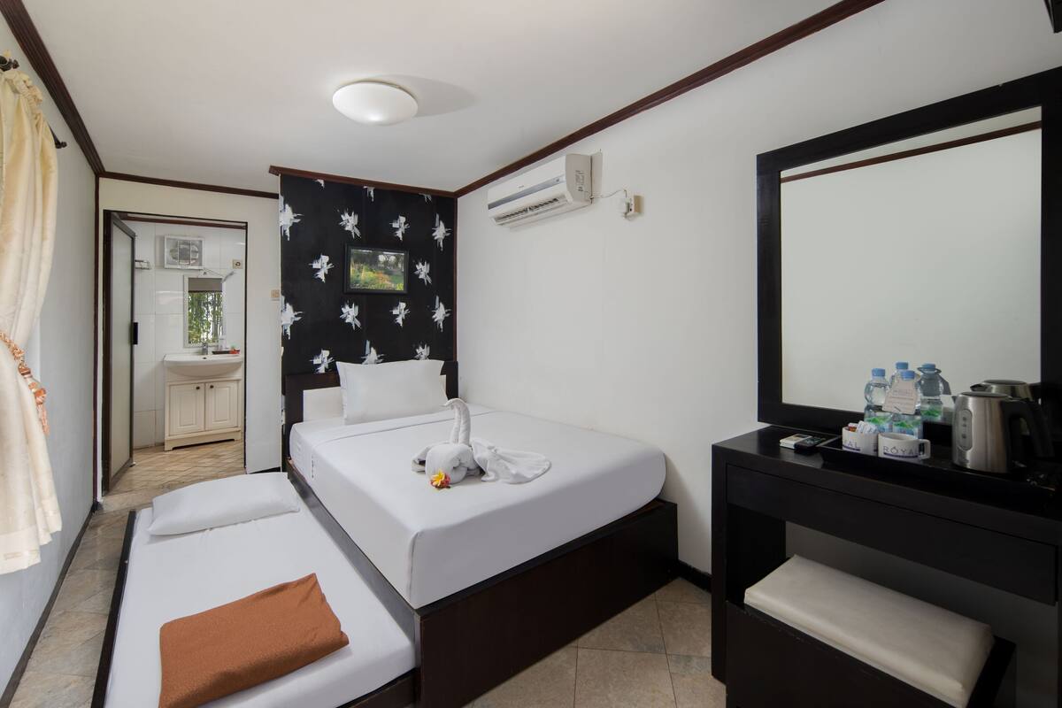 A hotel room with a bed, a bedside table, a mirror, and a bathroom visible through an open door.