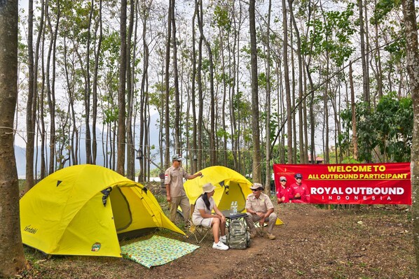 A campsite with yellow tents, a welcome banner, and a forested backdrop.