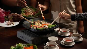 A hot pot setup with various vegetables and meats, surrounded by bowls of sauces and a portable heater.