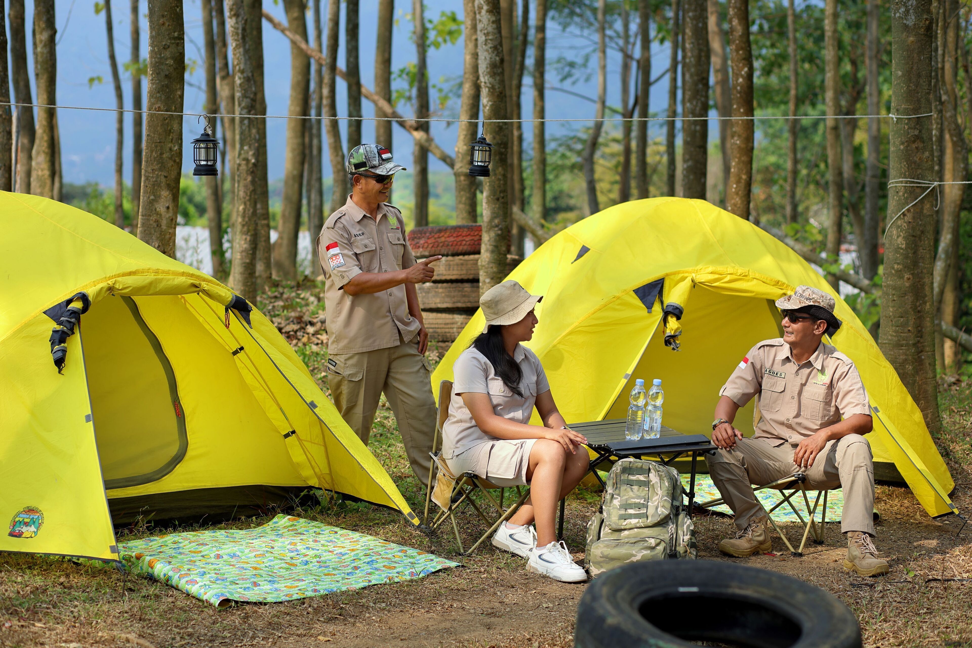 Two yellow tents set up in a forest with a table between them.