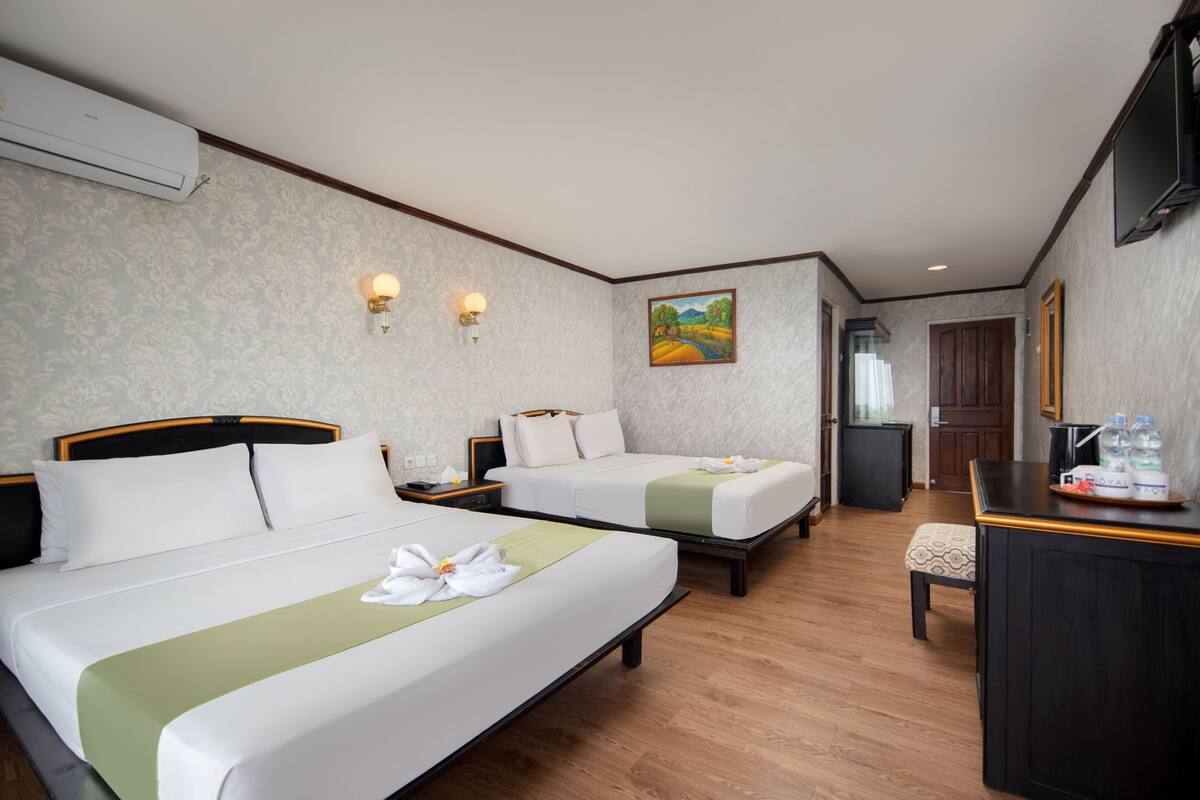 A hotel room with two beds, a desk, a television, and a painting on the wall.