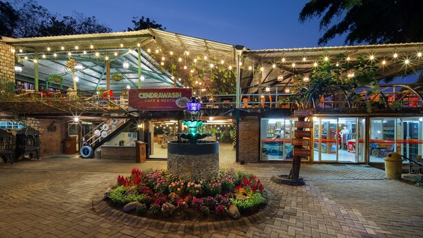 A cafe and restaurant with outdoor seating, a fountain, and a sign for 'CENDRAWASH'. - Royal Caravan Hotel Trawas (Trawas)