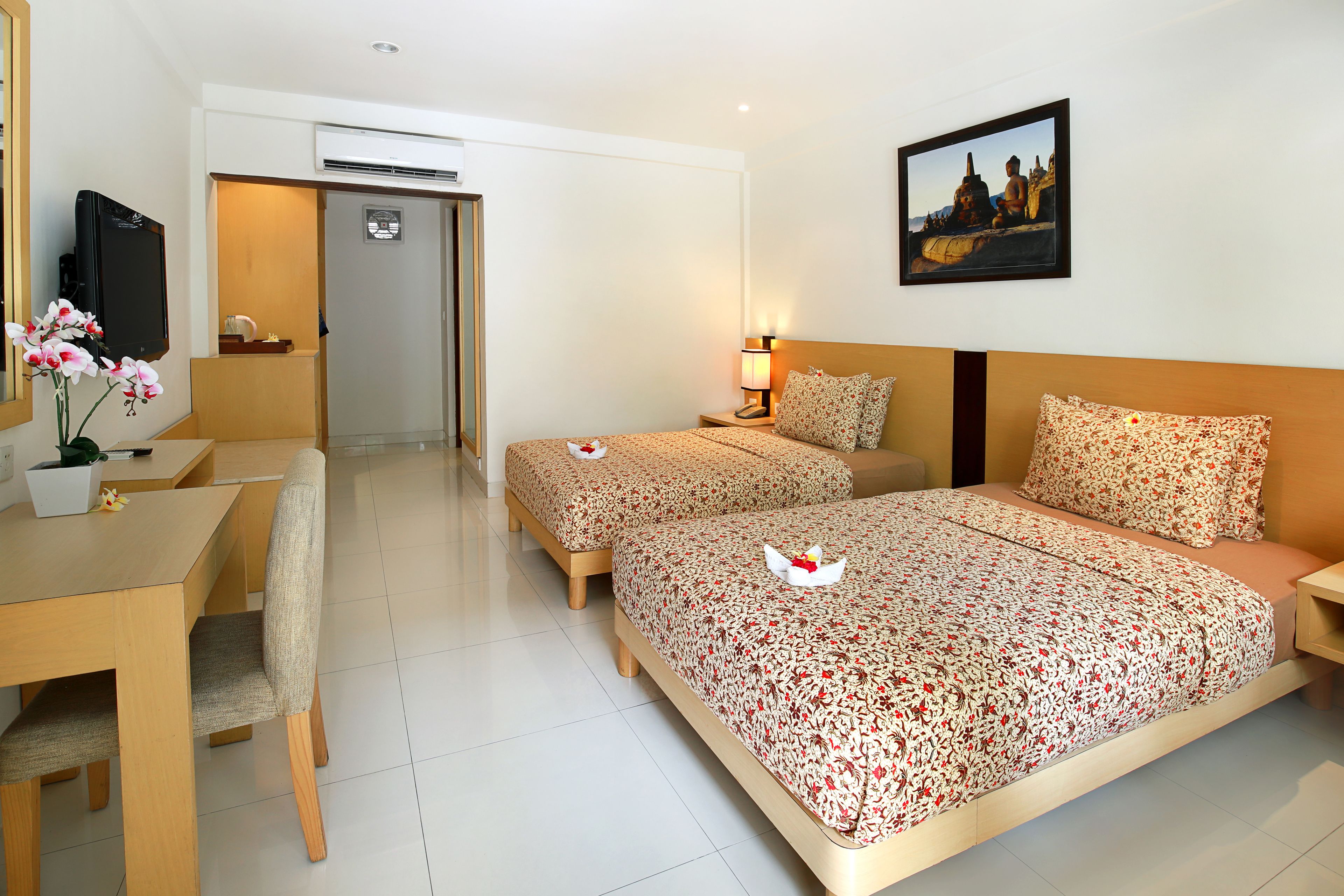 A hotel room with two beds, a desk, a chair, a TV, and a framed picture on the wall.
