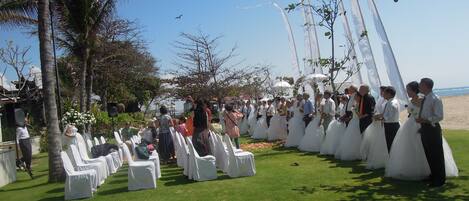 A wedding ceremony outdoors with guests seated on white chairs arranged in rows.