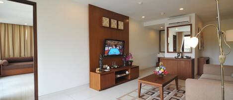 Una sala de estar moderna con una televisión de pantalla plana, mueble de madera para equipo electrónico, sofá, mesa de centro y una lámpara de pie.