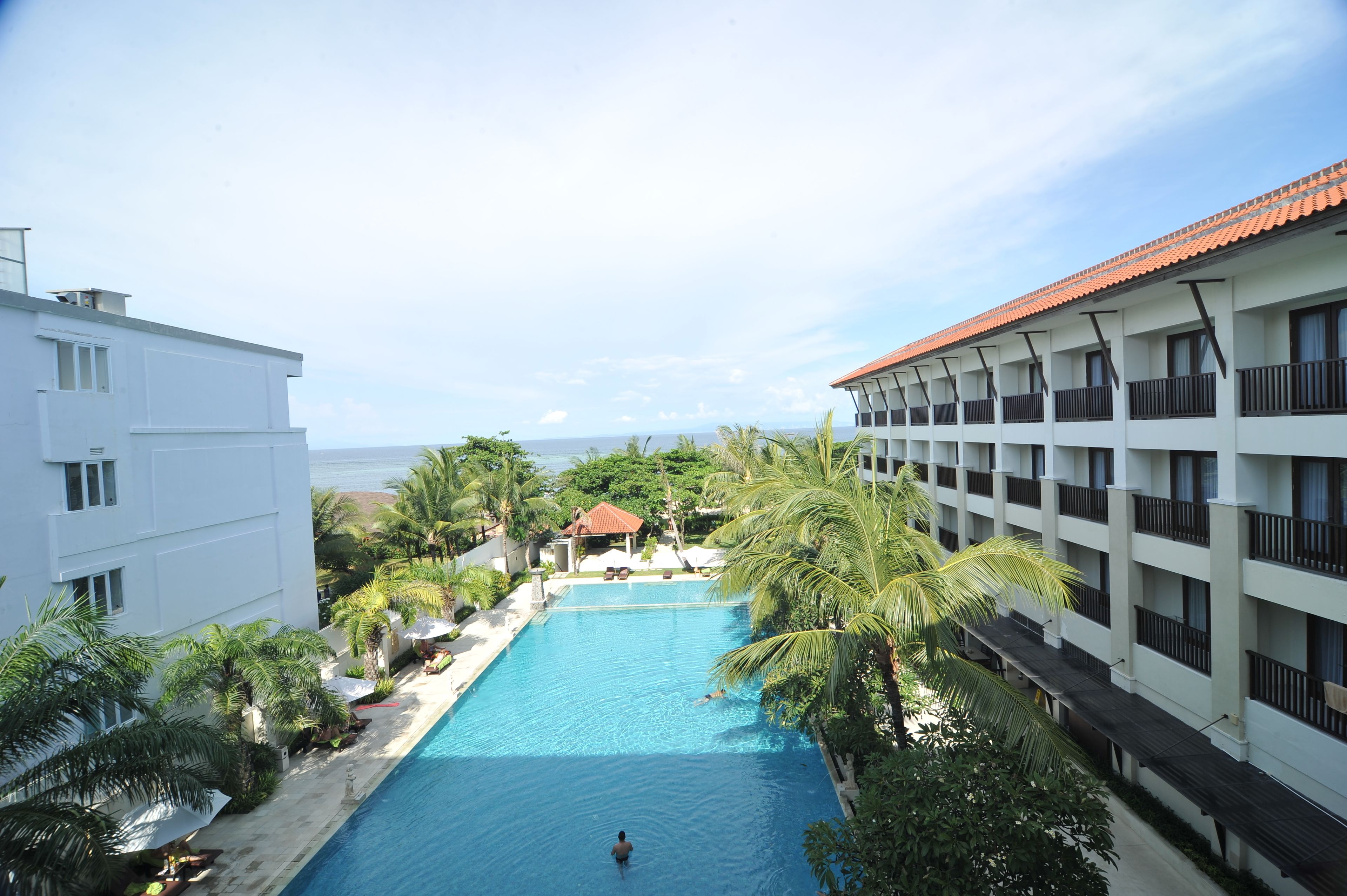 Un hotel con piscina rodeado de palmeras y vistas al mar.