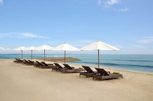 Une plage bordée de rangées de chaises longues et d’ombrelles blanches.