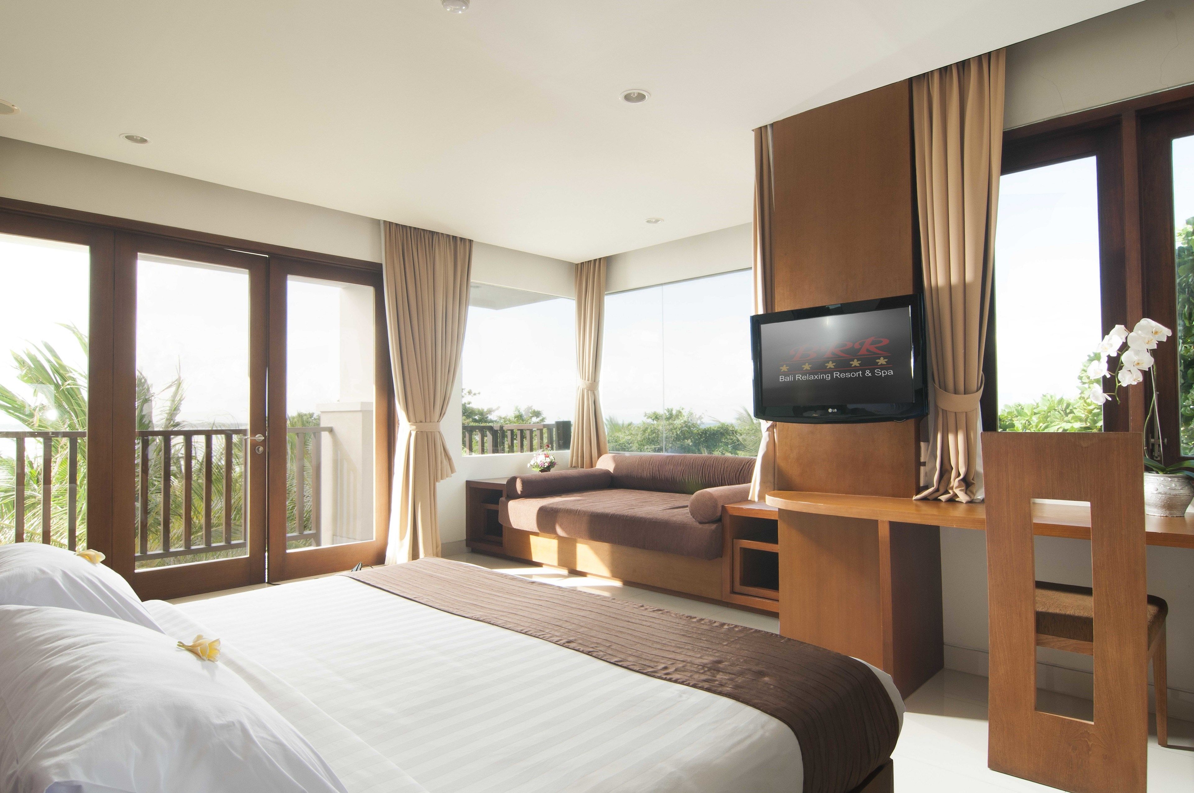 A hotel room with a large bed, a sofa, a TV, and a balcony with curtains.