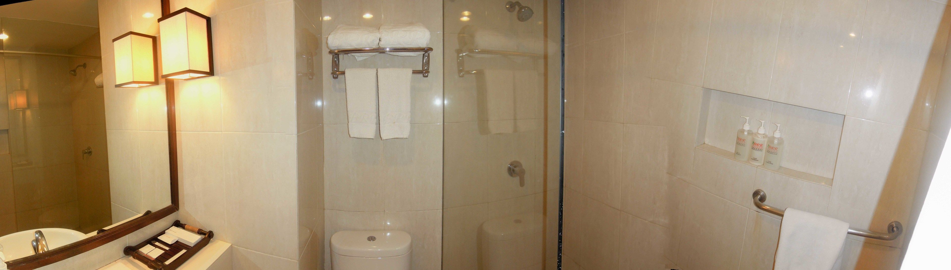 Un baño moderno con ducha envuelta en vidrio, un lavamanos con espejo y un estante con artículos de aseo.