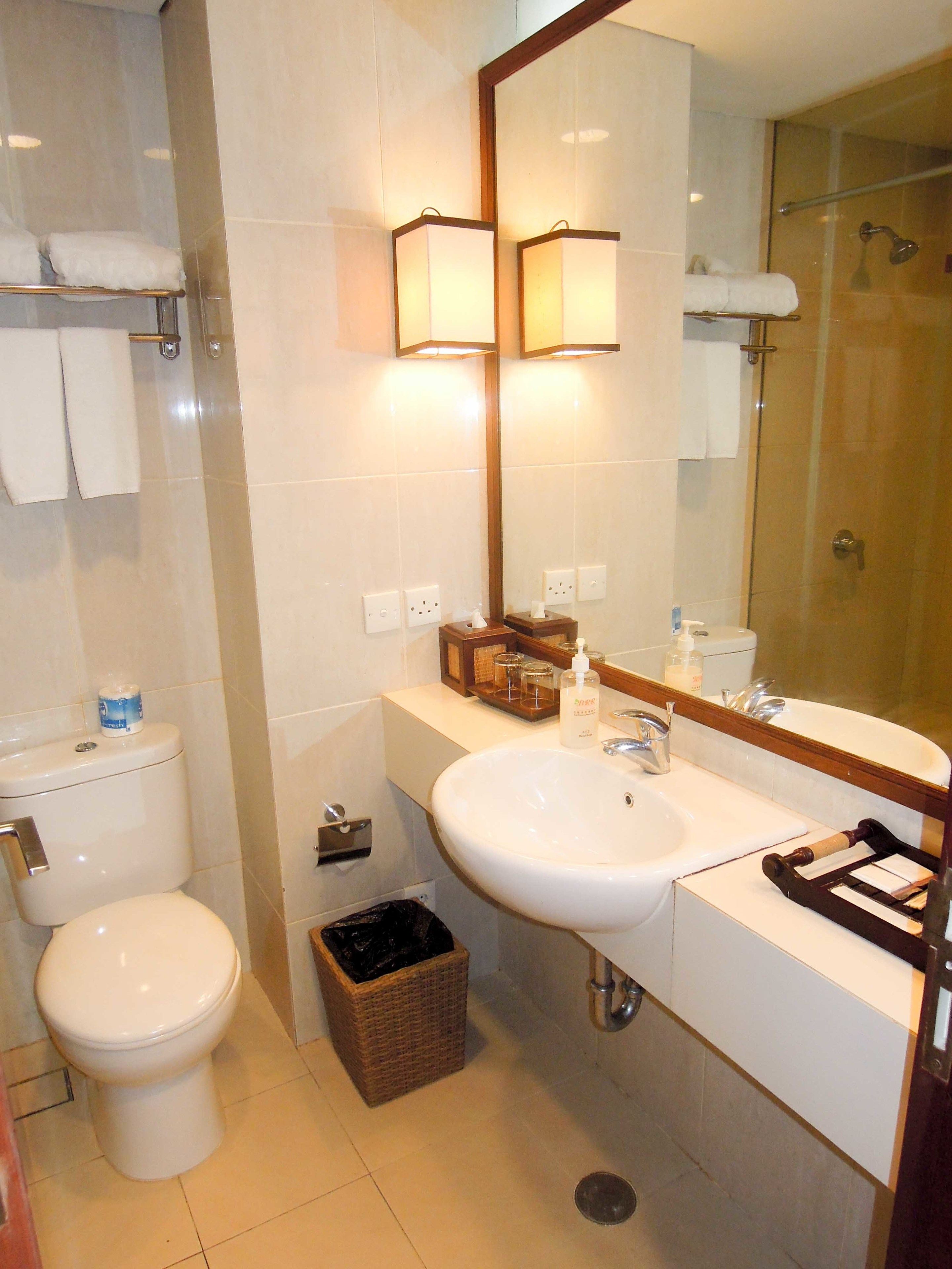 A bathroom with a toilet, sink, mirror, and shower.