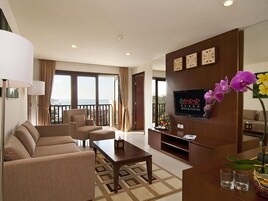 A modern hotel room with a sofa, a coffee table, a TV mounted on a wooden wall, and a balcony with a view.