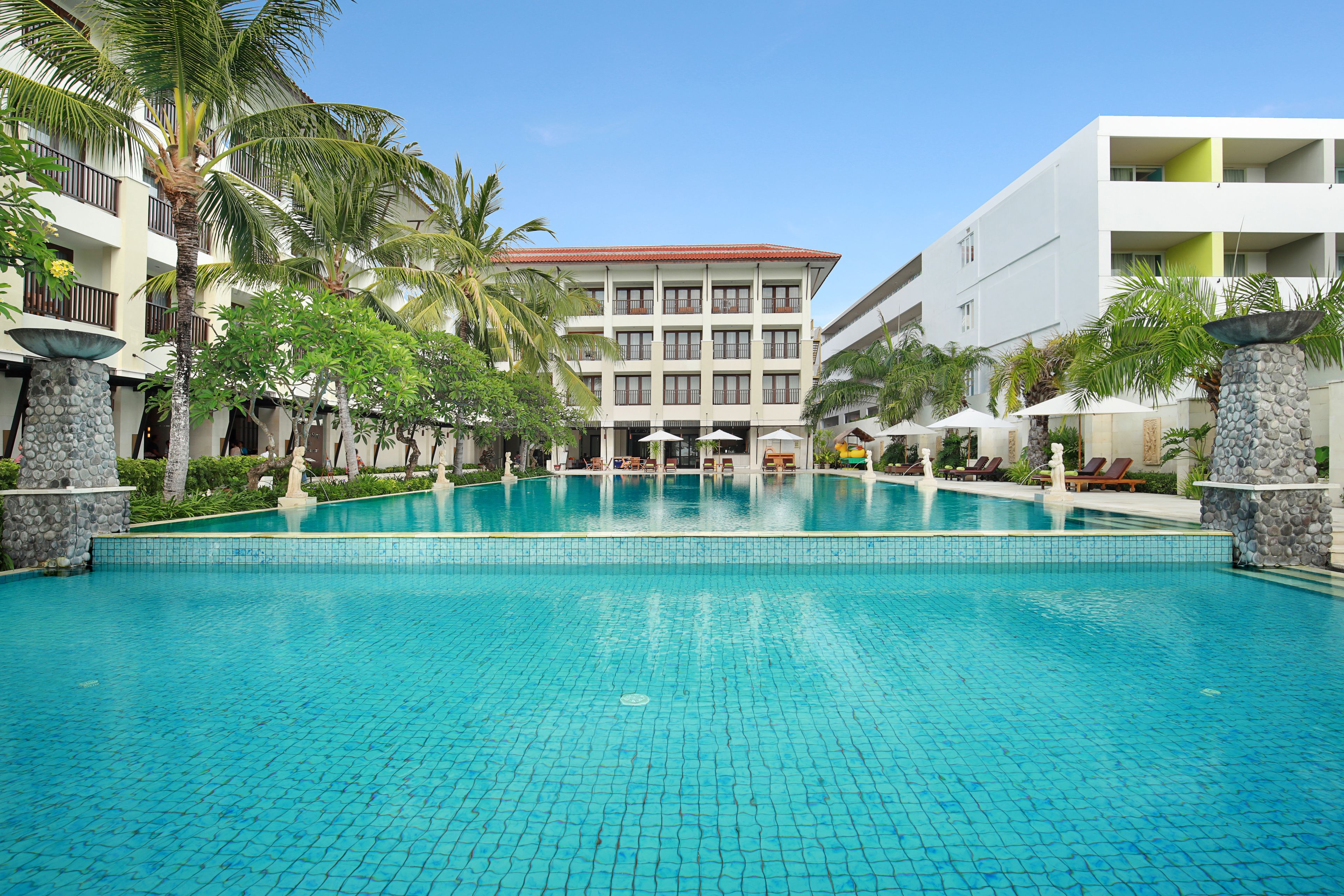 Un hotel con piscina, palmeras y un edificio de varios pisos con balcones.