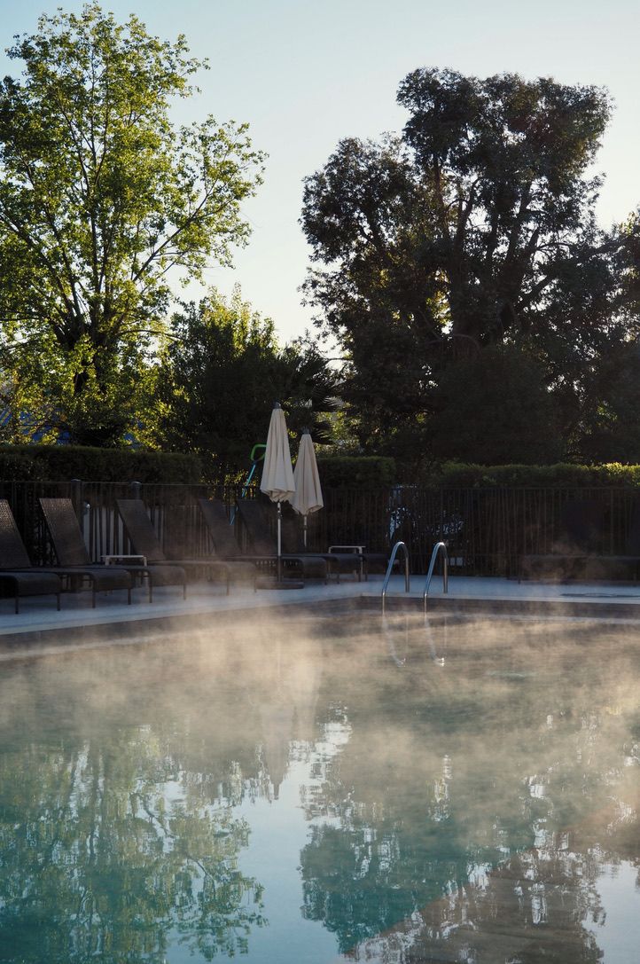 A hot tub surrounded by lounge chairs and umbrellas, with trees in the background.