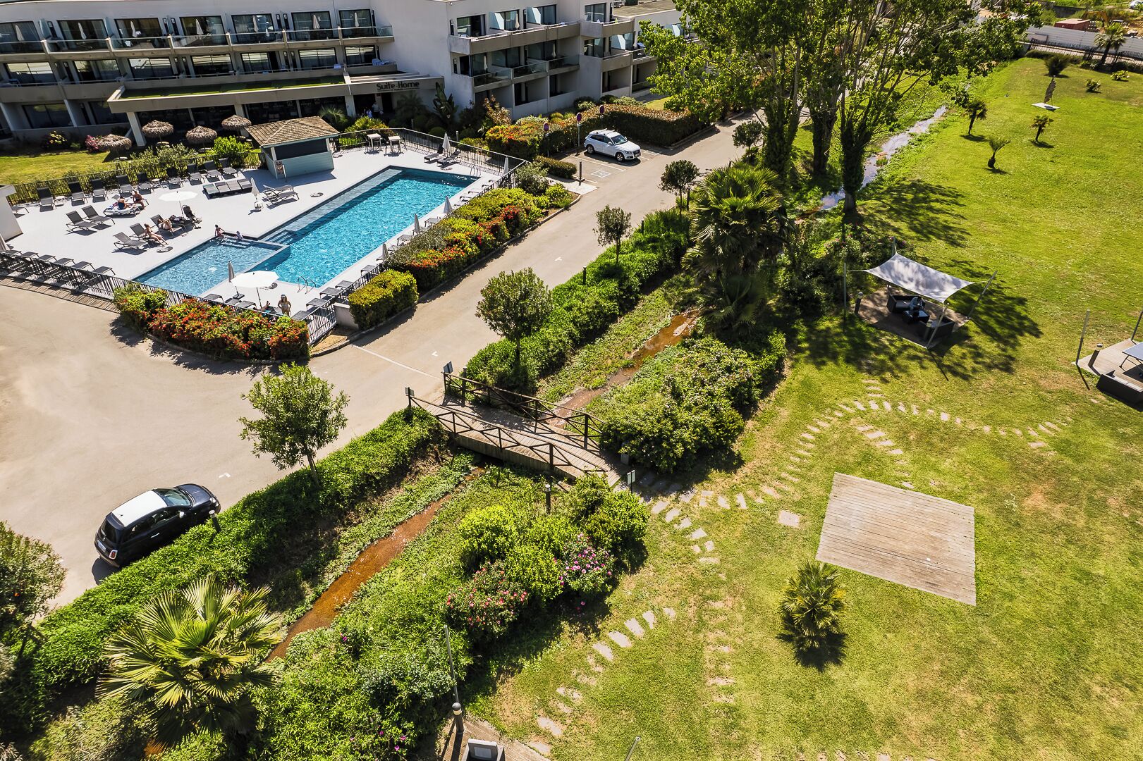 An aerial view of a hotel with a swimming pool, lounge chairs, and a well-maintained garden.