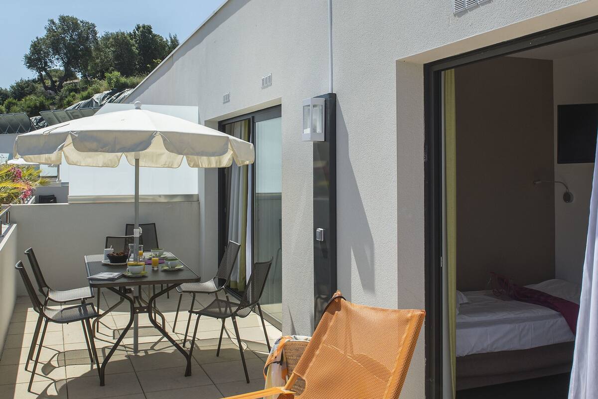 Ein modernes Hotelzimmer mit Balkon, einem Esstisch und Stühlen sowie einem großen Sonnenschirm.