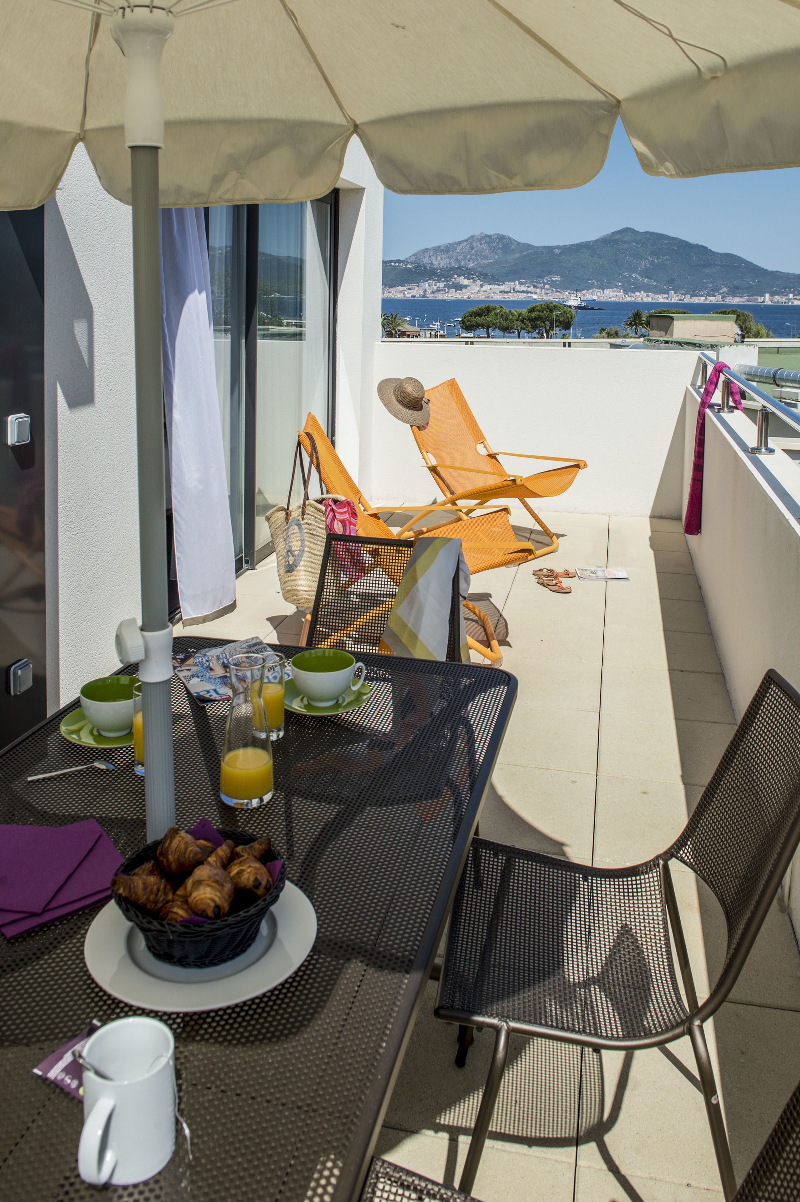 Eine Terrasse mit Tisch, gedeckt für ein Frühstück, darunter Croissants, Saft und eine Kaffeetasse.