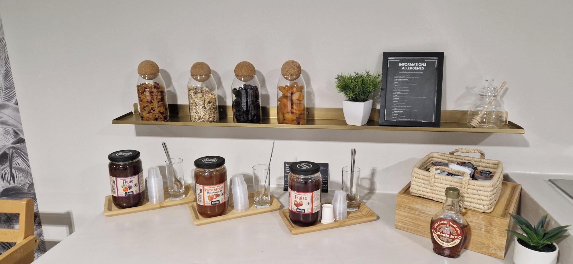 Un comptoir de cuisine avec divers pots de confitures, un panneau indiquant les allergènes et un panier rempli d’articles divers.