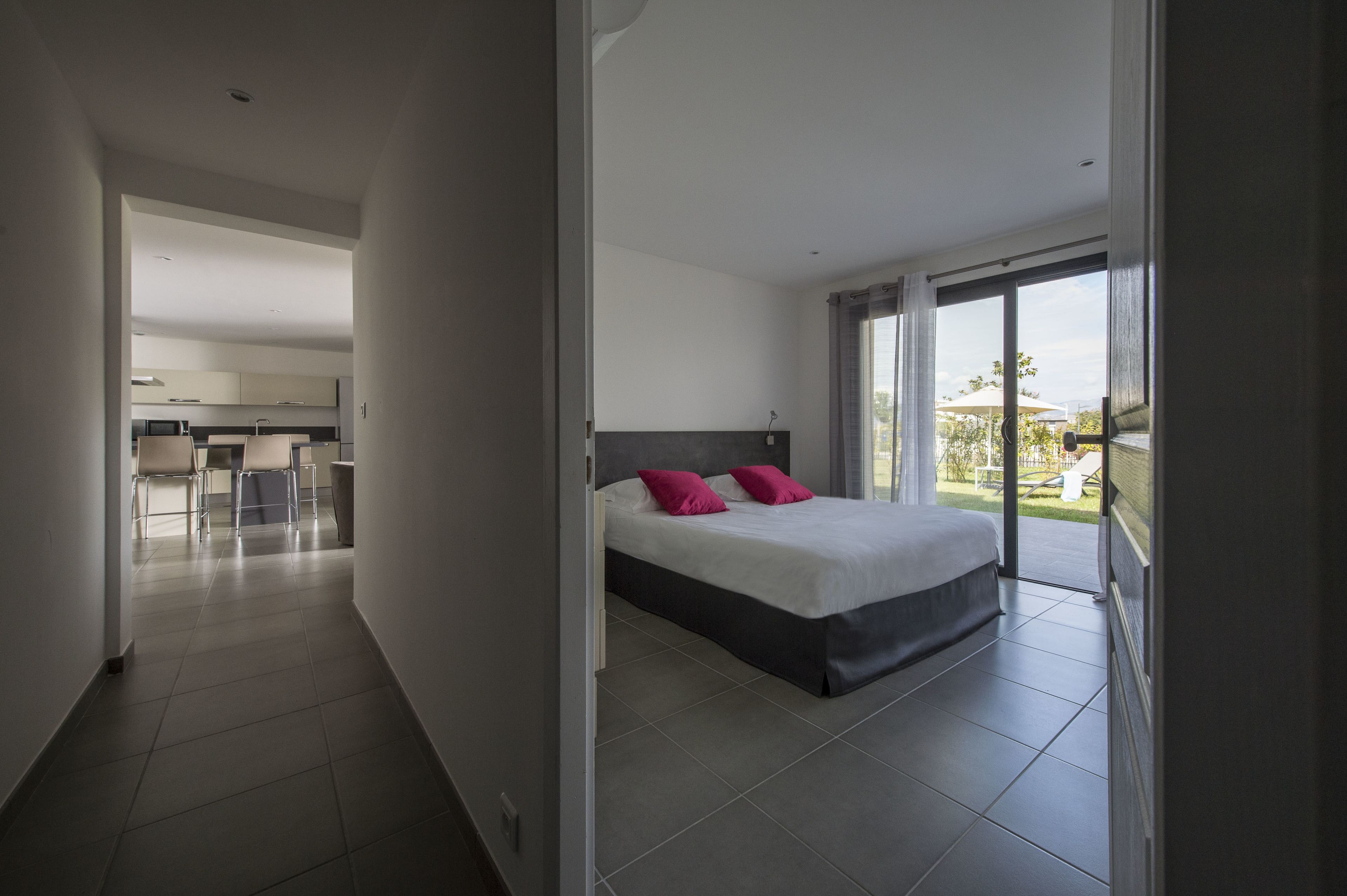 A modern hotel room with a large bed, a balcony with a view, and a separate dining area.