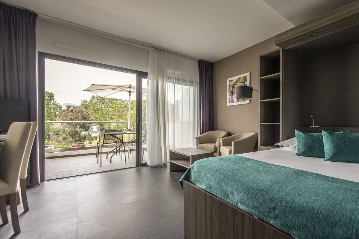 Ein Hotelzimmer mit einem großen Bett, einem Schreibtisch, einem Stuhl und einem Balkon mit Sonnenschirm.