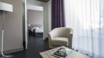 Una habitación de hotel con cama, una silla, una mesa con una revista y una lámpara.