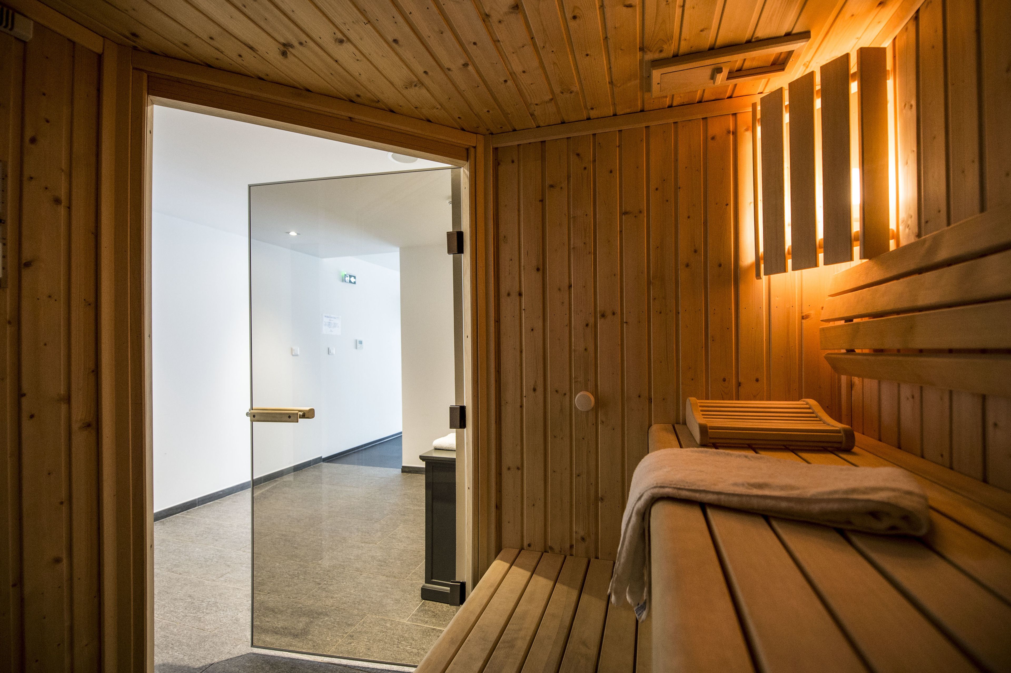 A sauna room with wooden walls and benches, a towel on one bench, and a door leading to another room.