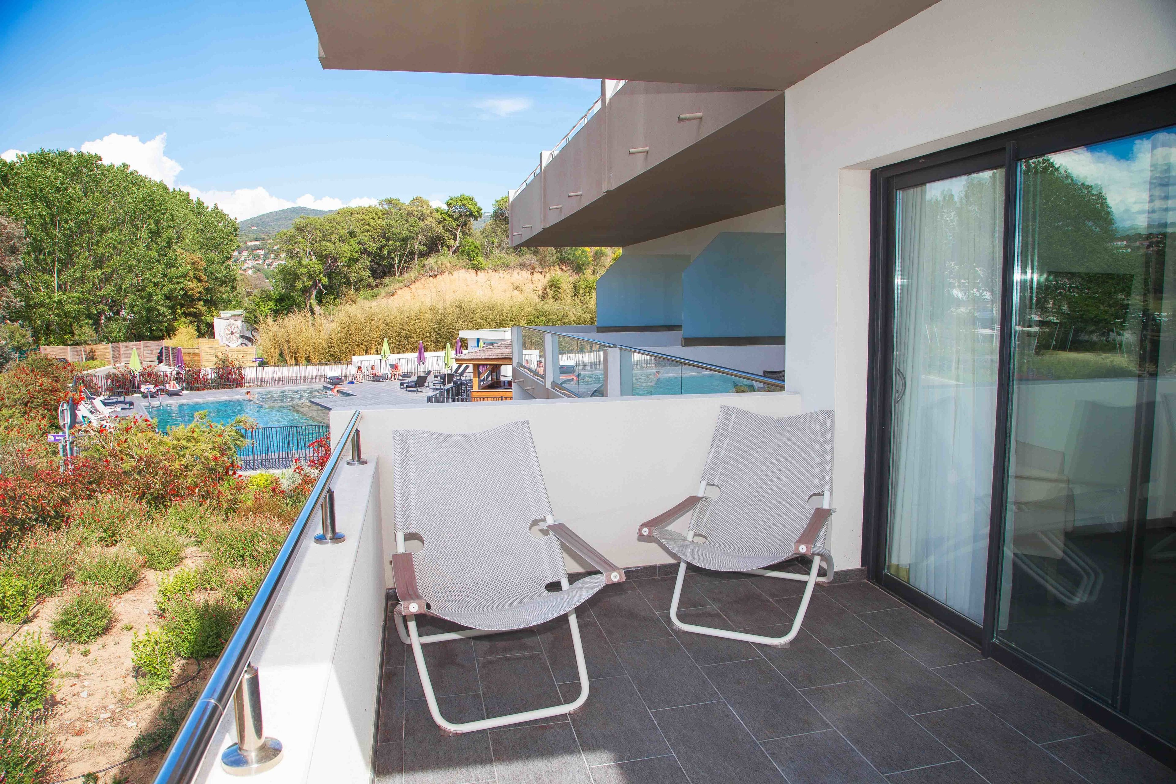 A balcony with two chairs, a pool, and a view of the surrounding landscape.