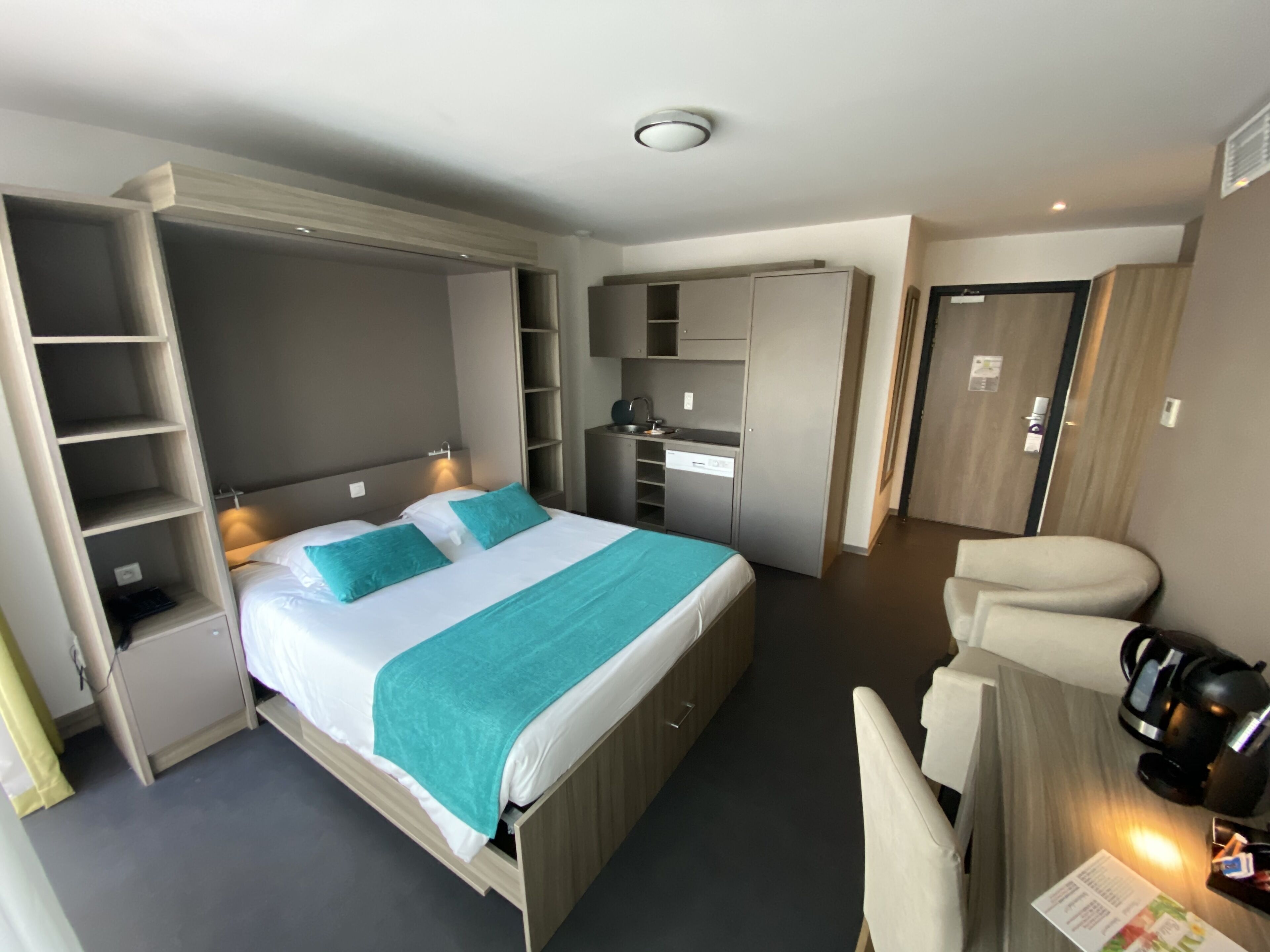 Une chambre d’hôtel moderne équipée d’un lit, d’une armoire intégrée et d’un coin salon avec une machine à café.