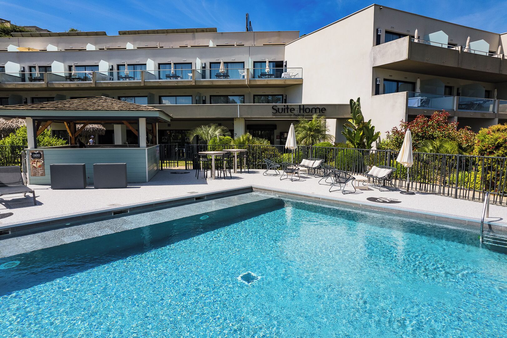 A hotel with a swimming pool, outdoor seating, and a 'Suite Home' sign.