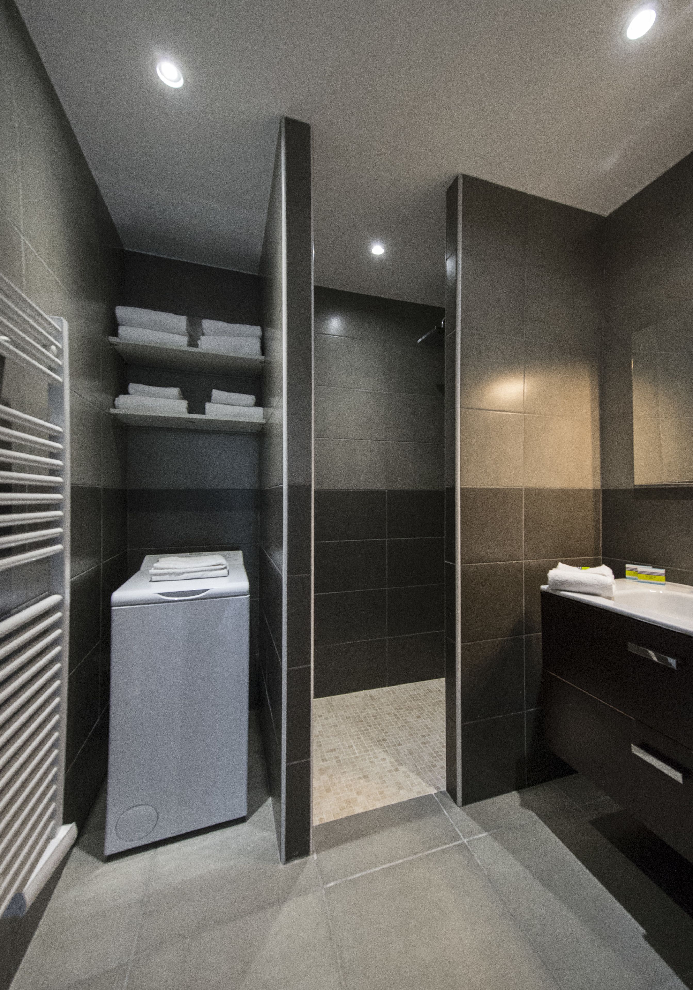 A modern bathroom with a walk-in shower, a built-in laundry machine, and a vanity with a mirror.