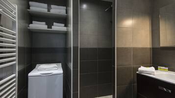 A modern bathroom with a walk-in shower, a built-in laundry machine, and a vanity with a mirror.