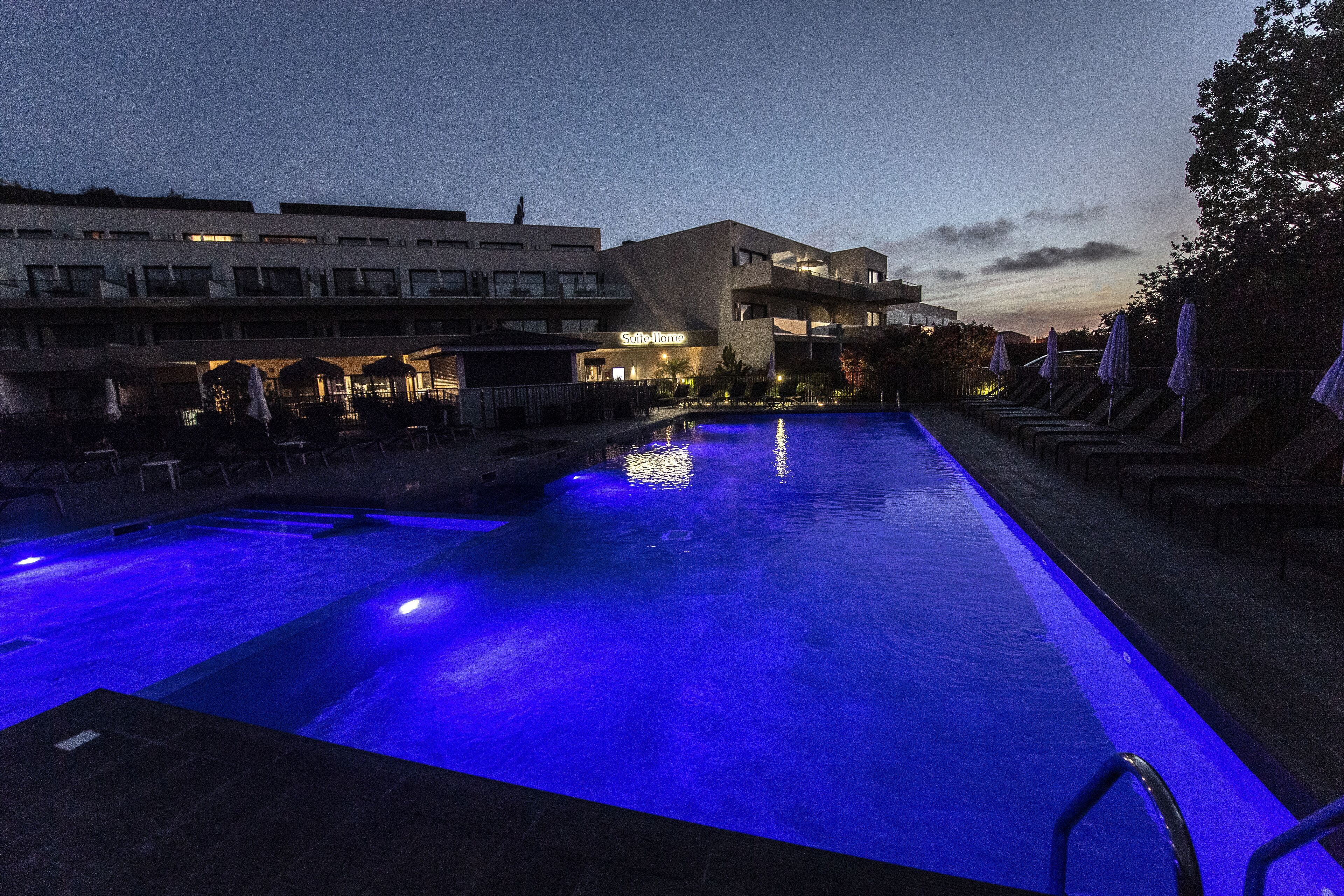 Una piscina con iluminación azul, sillones de descanso y un edificio con un letrero que dice "Soleil Home".