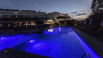 Una piscina con iluminación azul, sillones de descanso y un edificio con un letrero que dice "Soleil Home".