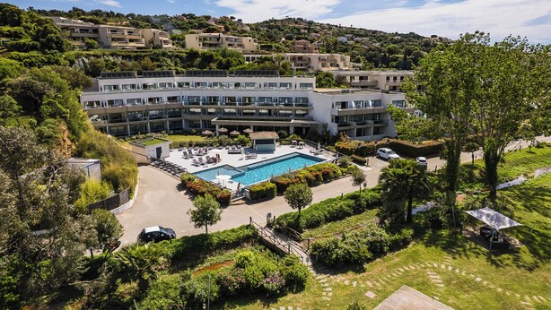 Un hotel amb piscina, múltiples balcons i vegetació abundant.