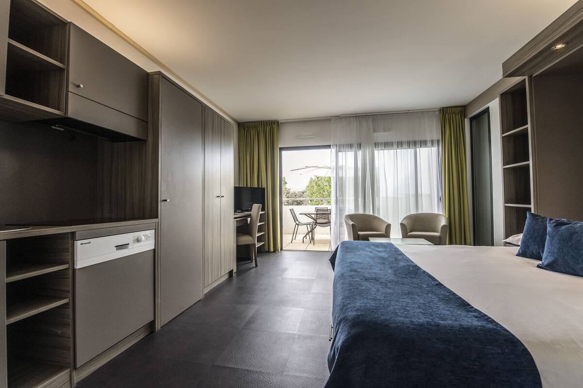 Ein Hotelzimmer mit einem Bett, einem Schreibtisch, einem Stuhl und einem Balkon mit Tisch und Stühlen.