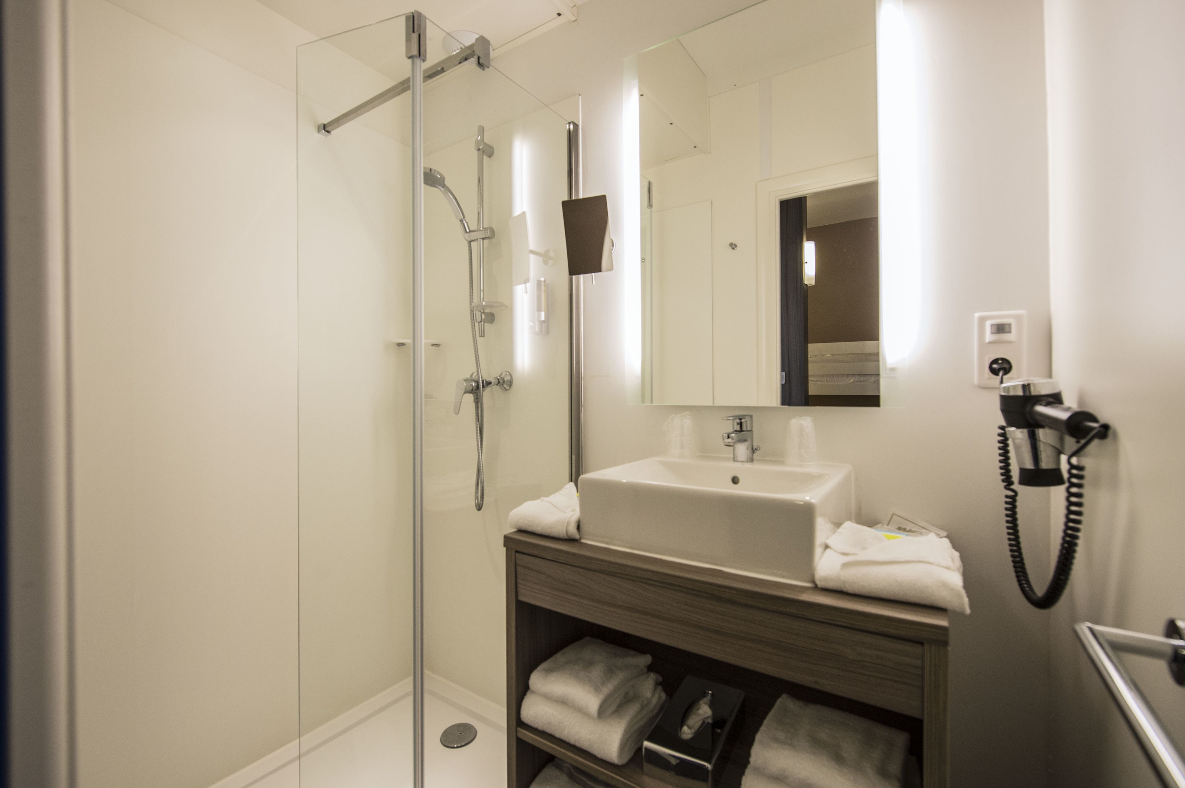 Un baño moderno con ducha de vidrio, lavamanos blanco y espejo sobre él.