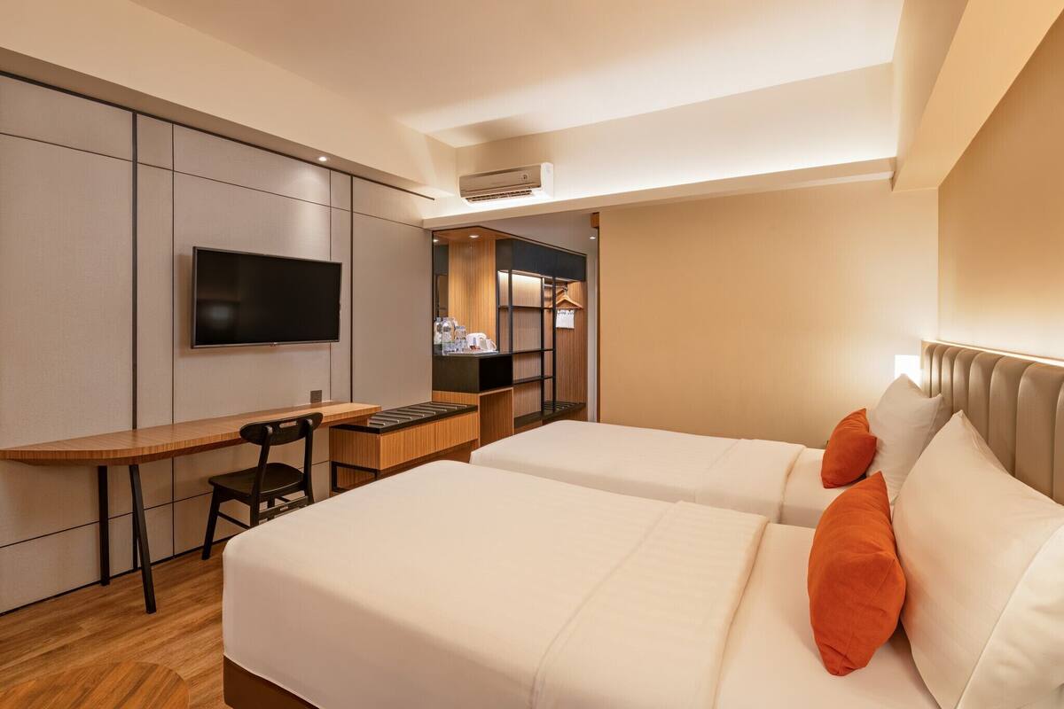 A hotel room with a bed, a desk, a chair, a TV, and a kitchenette.