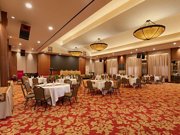 A banquet hall with round tables, chairs, and a red carpet.