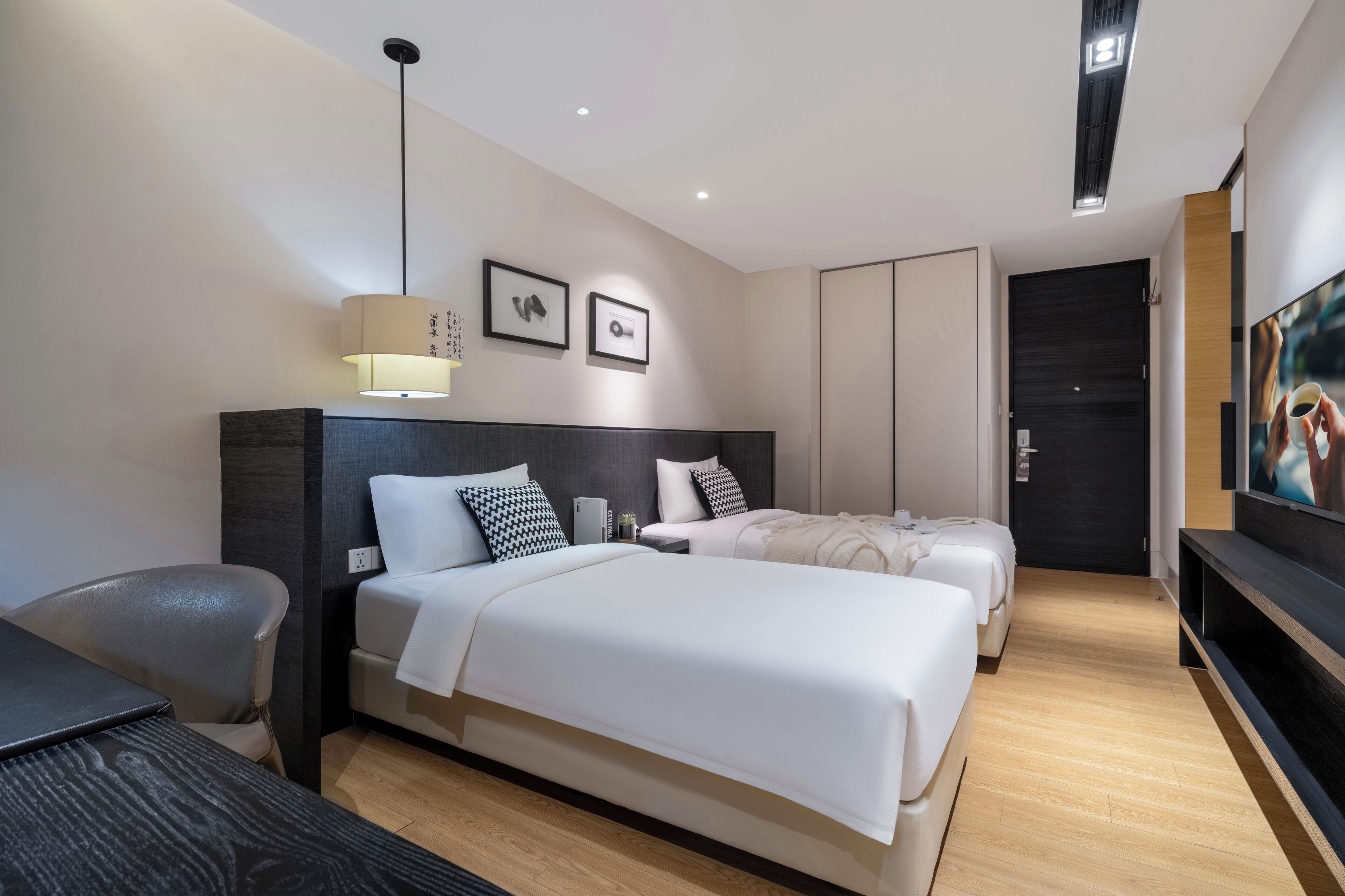 A modern hotel room with two beds, a desk, a chair, a TV, and a large painting on the wall.