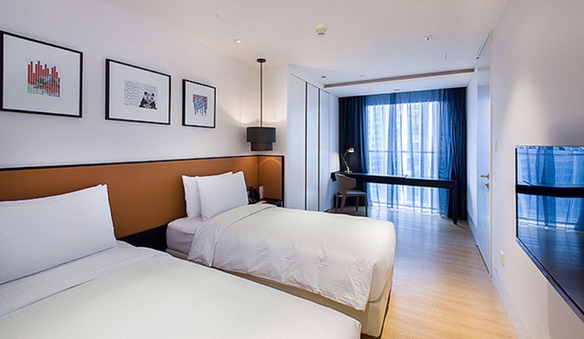 A hotel room with two beds, a desk, a chair, and a large window with curtains.
