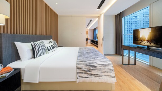 Een moderne hotelkamer met een groot bed, een televisie en uitzicht op de stad door grote ramen.