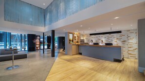Een ruime lobby met een receptiebalie, zithoek en een hoog plafond met verticale lijnen.