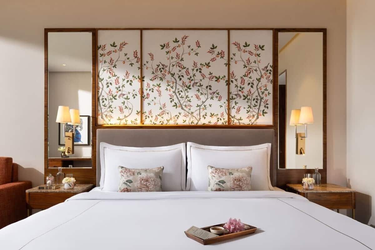 A hotel room with a large bed, two bedside tables with lamps, a large mirror, and a decorative panel above the bed.