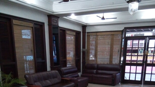 A spacious lobby with a large, dark brown leather sofa set, a potted plant, and a tiled floor. - YMCA International House (Kanayannur)