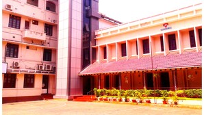 A multi-story building with a central tower, multiple balconies, and a covered entrance area with potted plants. - YMCA International House (Kanayannur)