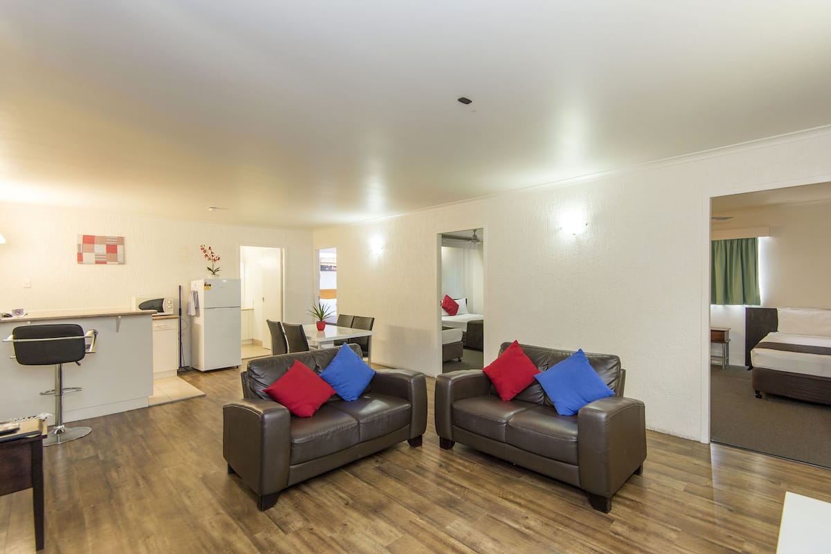 A modern living room with two leather sofas, a small kitchen area, and a separate bedroom with a bed.