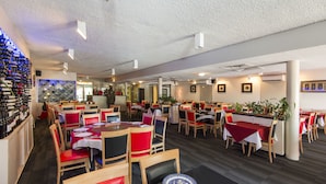 A restaurant with multiple dining tables and chairs, a wine rack on the left, and framed pictures on the walls. - Coral Sands Motel (Mackay)